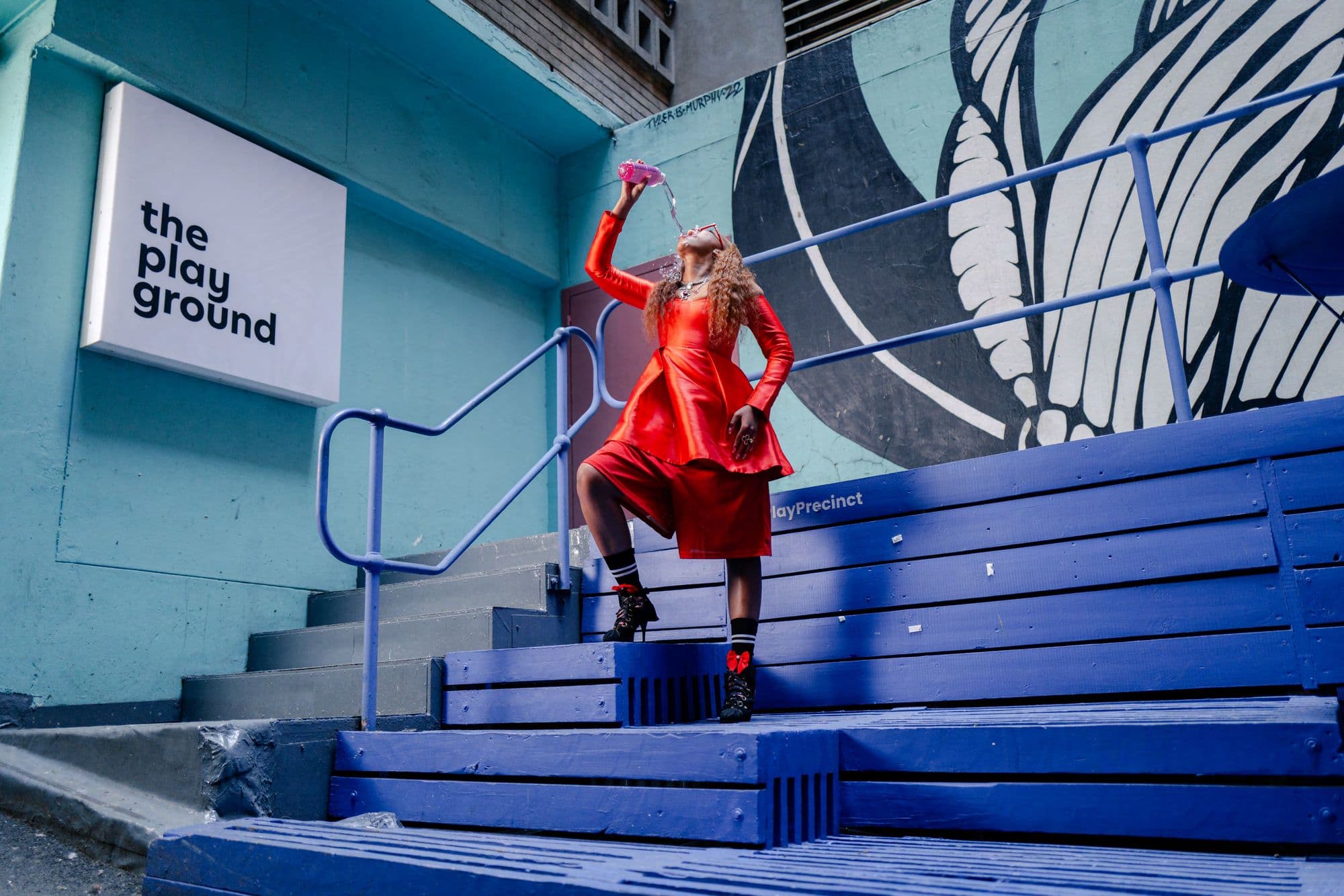 Person in a red outfit pours water from a pink bottle on blue wooden steps.