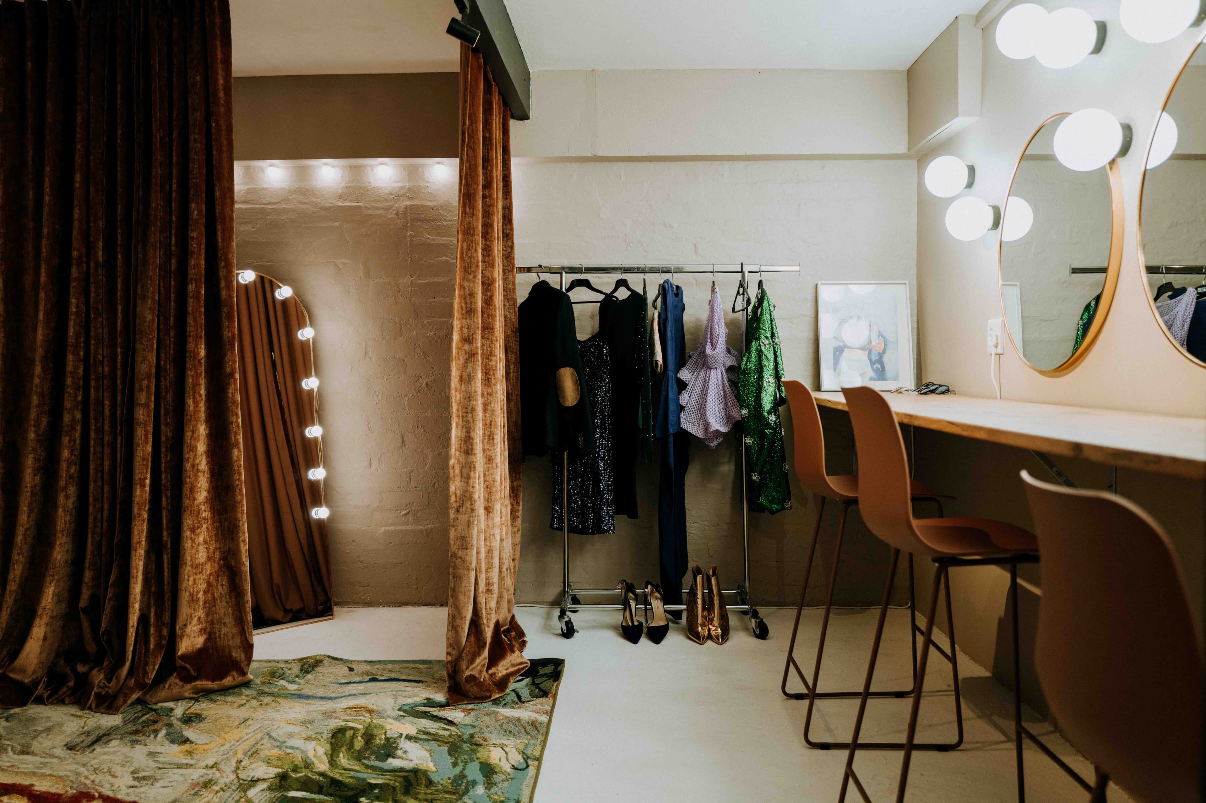 Dressing room with brown velvet curtains, a clothing rack, and a vanity with round mirrors.
