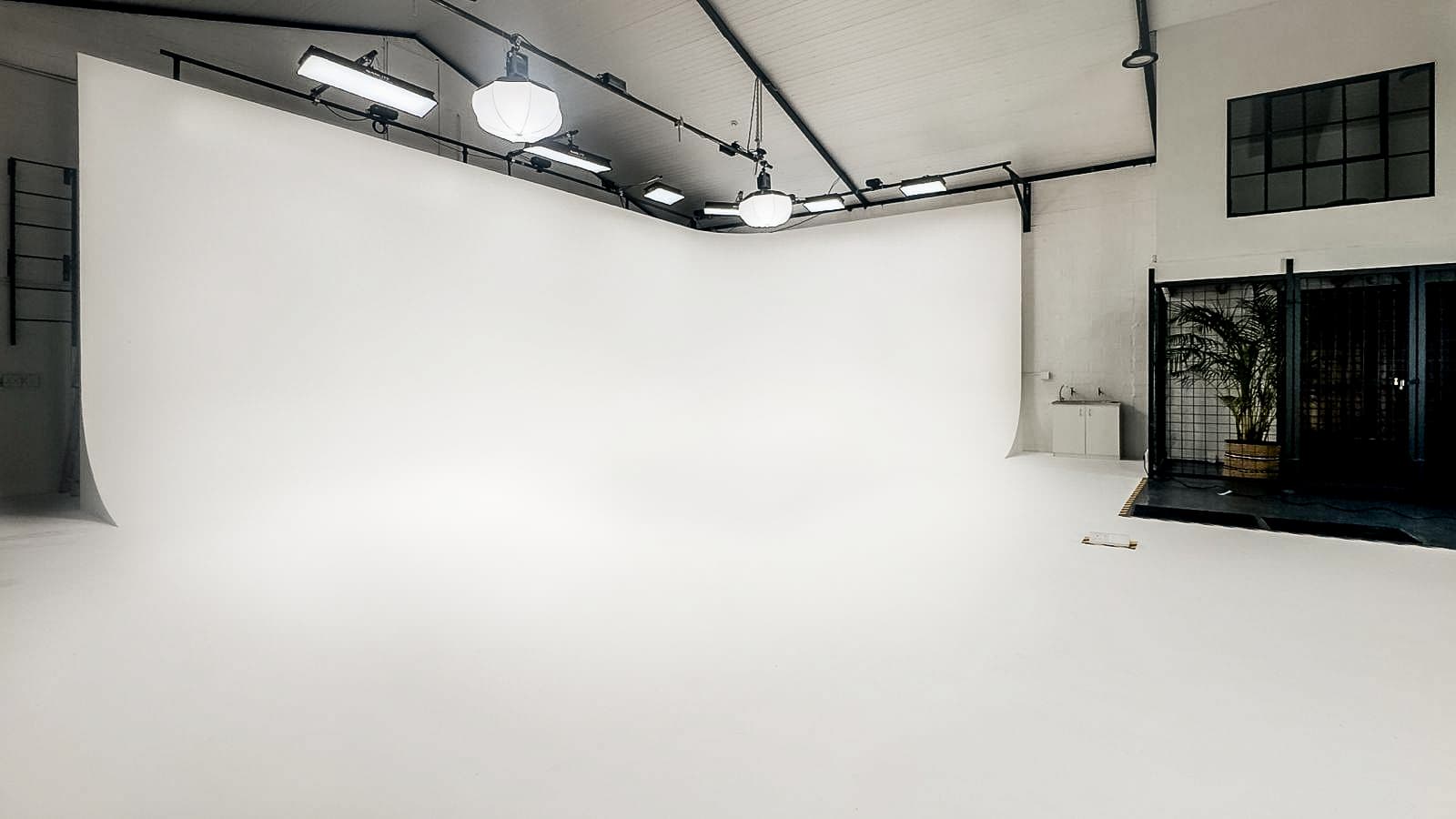 Bright professional photography studio featuring a large white infinity cove and overhead studio lighting.
